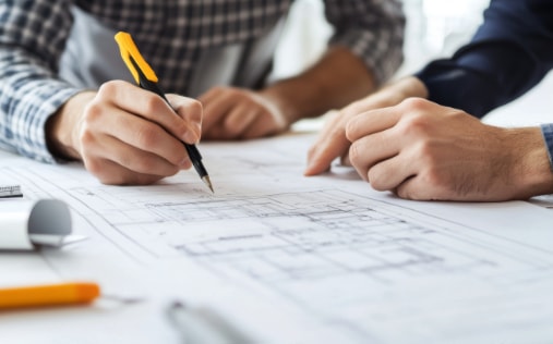 Zwei Personen arbeiten gemeinsam an Architektur- oder Bauzeichnungen, Nahaufnahme von Händen und Stift auf dem Plan