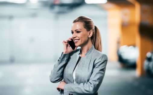 Lächelnde Geschäftsfrau im grauen Anzug telefoniert in einer Tiefgarage